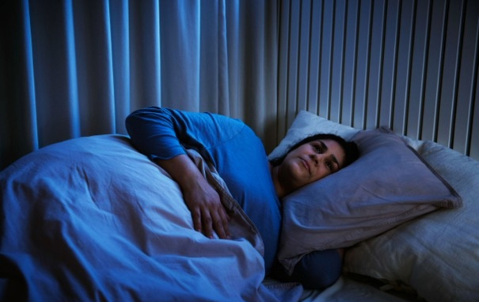 Person lying awake in bed at night under a white duvet in a dimly lit bedroom.